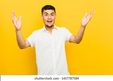 Young Hispanic Man Receiving A Pleasant Surprise, Excited And Raising Hands.