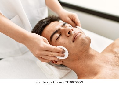 Young hispanic man relaxed having facial treatment cleaning face with cotton disk at beauty center - Shutterstock ID 2139929293