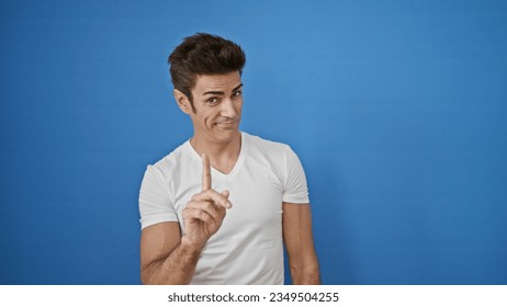 Young hispanic man saying no with finger smiling over isolated blue background