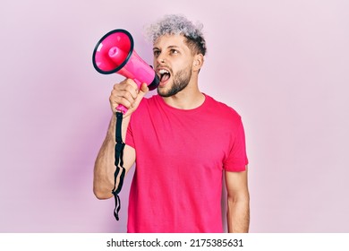 Young Hispanic Man Screaming With Megaphone Over Pink Background