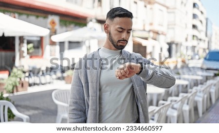 Young hispanic man with serious face looking watch at street