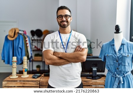 Young hispanic man shopkeeper smiling confident standing with arms crossed gesture at clothing store