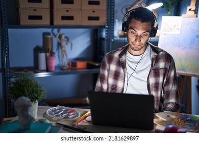 Young Hispanic Man Sitting At Art Studio With Laptop Late At Night Depressed And Worry For Distress, Crying Angry And Afraid. Sad Expression. 