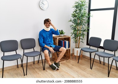 Young Hispanic Man Sitting At Doctor Waiting Room With Neck Injury Smiling Happy Doing Ok Sign With Hand On Eye Looking Through Fingers 