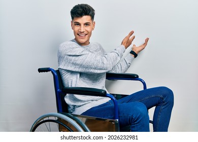 Young hispanic man sitting on wheelchair inviting to enter smiling natural with open hand  - Powered by Shutterstock