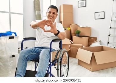 Young Hispanic Man Sitting On Wheelchair At New House Smiling In Love Showing Heart Symbol And Shape With Hands. Romantic Concept. 