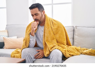 Young hispanic man sitting on sofa coughing at home - Powered by Shutterstock