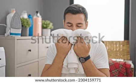 Young hispanic man smelling clothes at laundry room