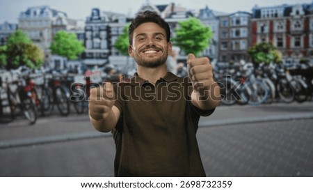 Young hispanic man smiling with bare hands forward miming a steering wheel on a busy street in amsterdam beside parked bicycles; joy travel exploration.