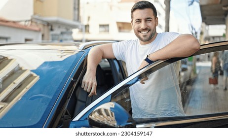 Young hispanic man smiling confident leaning on car door at street - Powered by Shutterstock