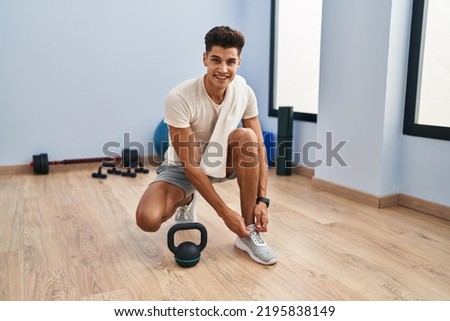 Young hispanic man smiling confident tying shoes at sport center