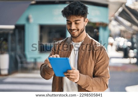 Young hispanic man smiling confident using touchpad at street