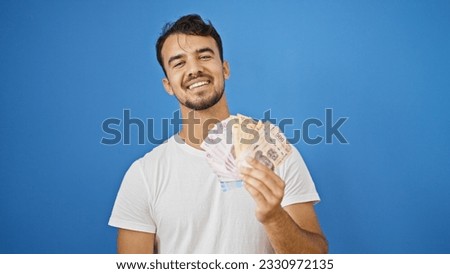 Young hispanic man smiling confident holding mexican pesos over isolated blue background