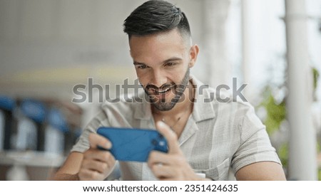 Young hispanic man smiling confident playing video game at coffee shop terrace