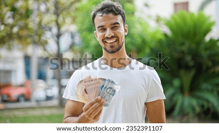 Young hispanic man smiling confident holding mexican pesos at park