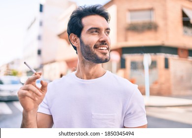 Young hispanic man smiling happy holding cigarette walking at the city. - Shutterstock ID 1850345494