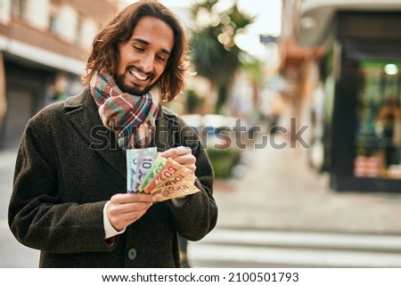 Young hispanic man smiling happy counting canadian dollars at the city.
