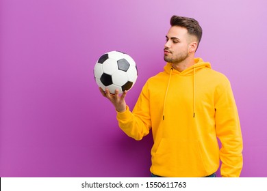 young hispanic man and soccer ball against purple background