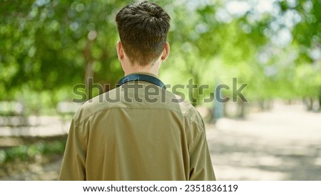 Young hispanic man standing backwards wearing headphones at park