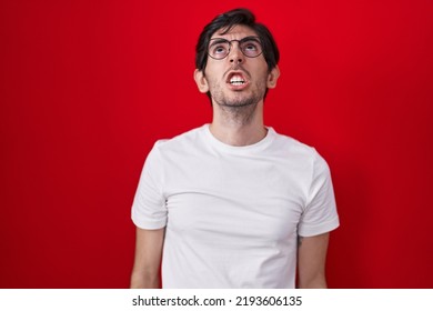 Young Hispanic Man Standing Over Red Background Angry And Mad Screaming Frustrated And Furious, Shouting With Anger. Rage And Aggressive Concept. 