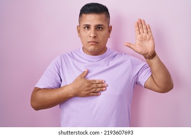 Young Hispanic Man Standing Over Pink Background Swearing With Hand On Chest And Open Palm, Making A Loyalty Promise Oath 