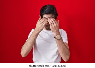 Young Hispanic Man Standing Over Red Background Rubbing Eyes For Fatigue And Headache, Sleepy And Tired Expression. Vision Problem 