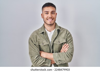 Young hispanic man standing over isolated background happy face smiling with crossed arms looking at the camera. positive person. 