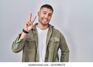 Young hispanic man standing over isolated background smiling looking to the camera showing fingers doing victory sign. number two.  - Shutterstock ID 2251398273