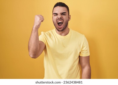 Young hispanic man standing over yellow background angry and mad raising fist frustrated and furious while shouting with anger. rage and aggressive concept.  - Shutterstock ID 2362438481