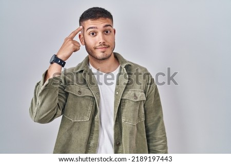 Young hispanic man standing over isolated background smiling pointing to head with one finger, great idea or thought, good memory 