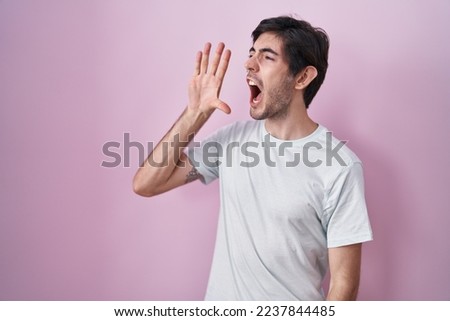 Young hispanic man standing over pink background shouting and screaming loud to side with hand on mouth. communication concept.  ストックフォト © 