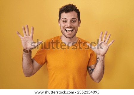 Young hispanic man standing over yellow background showing and pointing up with fingers number ten while smiling confident and happy. 