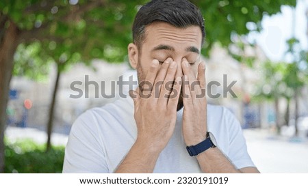 Young hispanic man standing with serious expression rubbing eyes at street