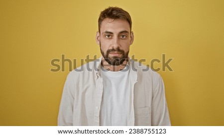 Young hispanic man standing with serious expression over isolated yellow background