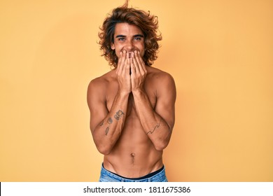 Young Hispanic Man Standing Shirtless Laughing And Embarrassed Giggle Covering Mouth With Hands, Gossip And Scandal Concept 