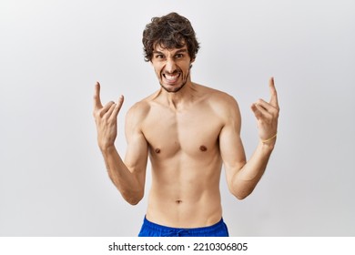 Young Hispanic Man Standing Shirtless Over Isolated, Background Shouting With Crazy Expression Doing Rock Symbol With Hands Up. Music Star. Heavy Concept. 