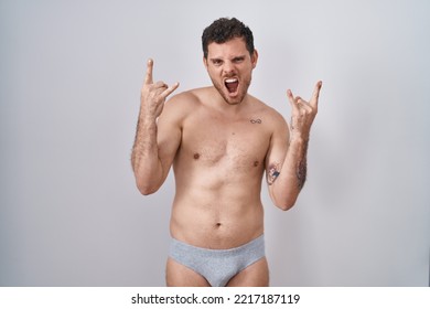 Young Hispanic Man Standing Shirtless Wearing Underware Shouting With Crazy Expression Doing Rock Symbol With Hands Up. Music Star. Heavy Music Concept. 