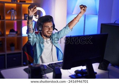 Young hispanic man streamer playing video game with winner expression at gaming room