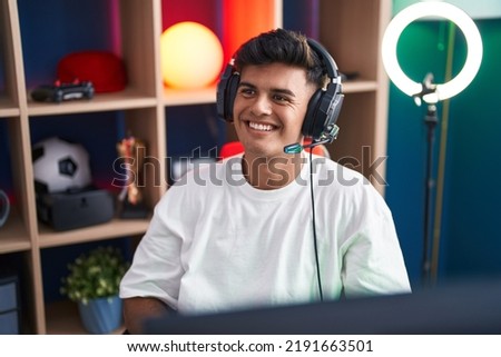 Young hispanic man streamer smiling confident sitting on table at gaming room