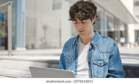 Young hispanic man student using laptop sitting on stairs at university