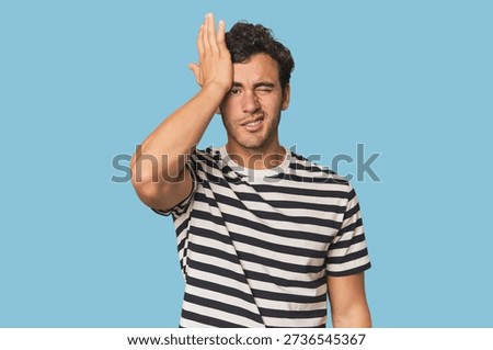 Young Hispanic man in studio forgetting something, slapping forehead with palm and closing eyes.