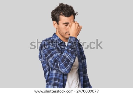 Young Hispanic man in studio having a head ache, touching front of the face.