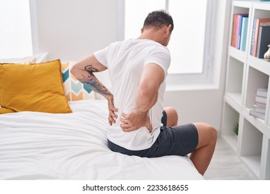 Young hispanic man suffering for back injury sitting on bed at bedroom
