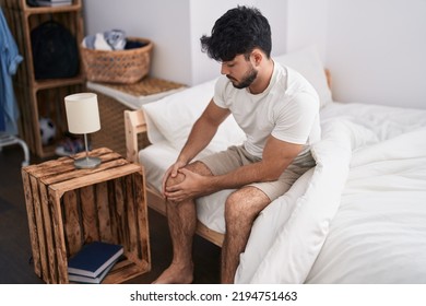 Young Hispanic Man Suffering For Knee Injury Sitting On Bed At Bedroom