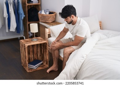 Young Hispanic Man Suffering For Knee Injury Sitting On Bed At Bedroom