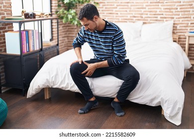 Young Hispanic Man Suffering For Knee Injury Sitting On Bed At Bedroom