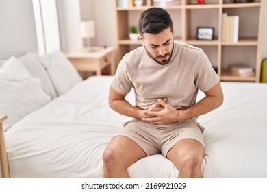 Young hispanic man suffering for stomachache sitting on bed at bedroom - Shutterstock ID 2169921029