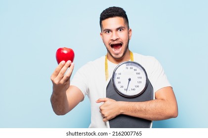 Young Hispanic Man Surprised Expression And Holding An Apple. Diet Concept