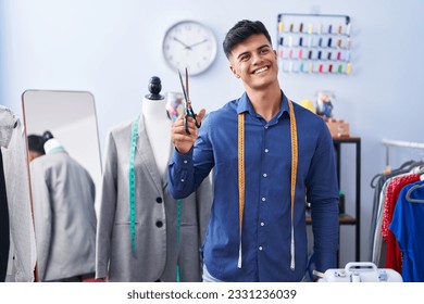 Young hispanic man tailor smiling confident holding scissors at clothing factory - Powered by Shutterstock