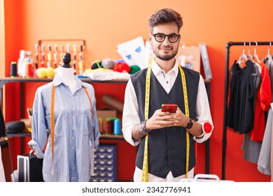 Young hispanic man tailor smiling confident using smartphone at atelier - Powered by Shutterstock